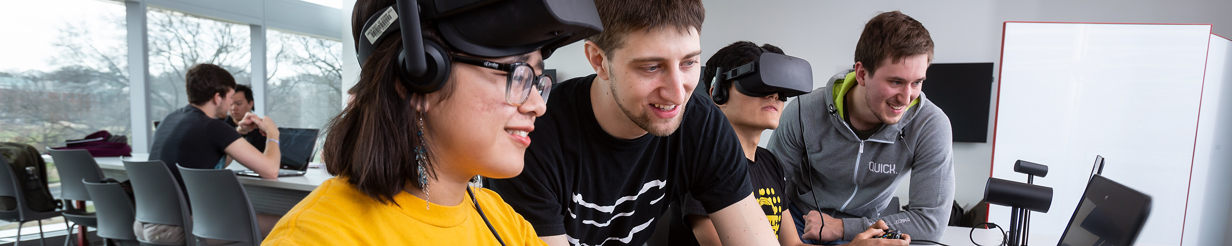 Several undergraduate students, two wearing virtual reality headsets, working in a classroom